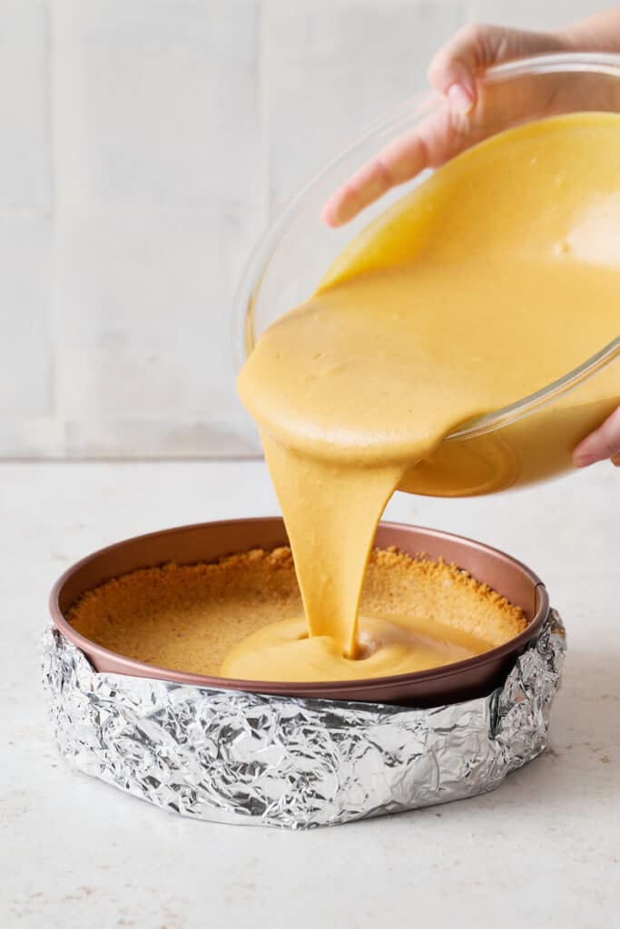 Pumpkin cheesecake batter being poured into a springform pan.