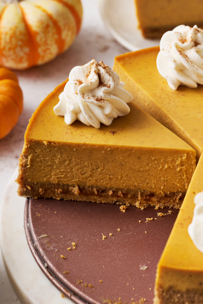 Slice of pumpkin cheesecake on spring form pan with whipped cream on top.