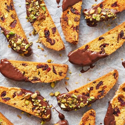 Cranberry orange biscotti dipping in chocolate and sprinkled with pistachios.