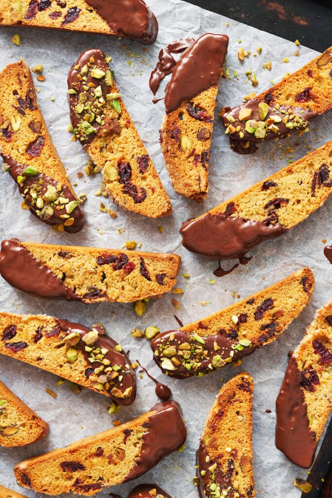 Cranberry orange biscotti dipping in chocolate and sprinkled with pistachios.