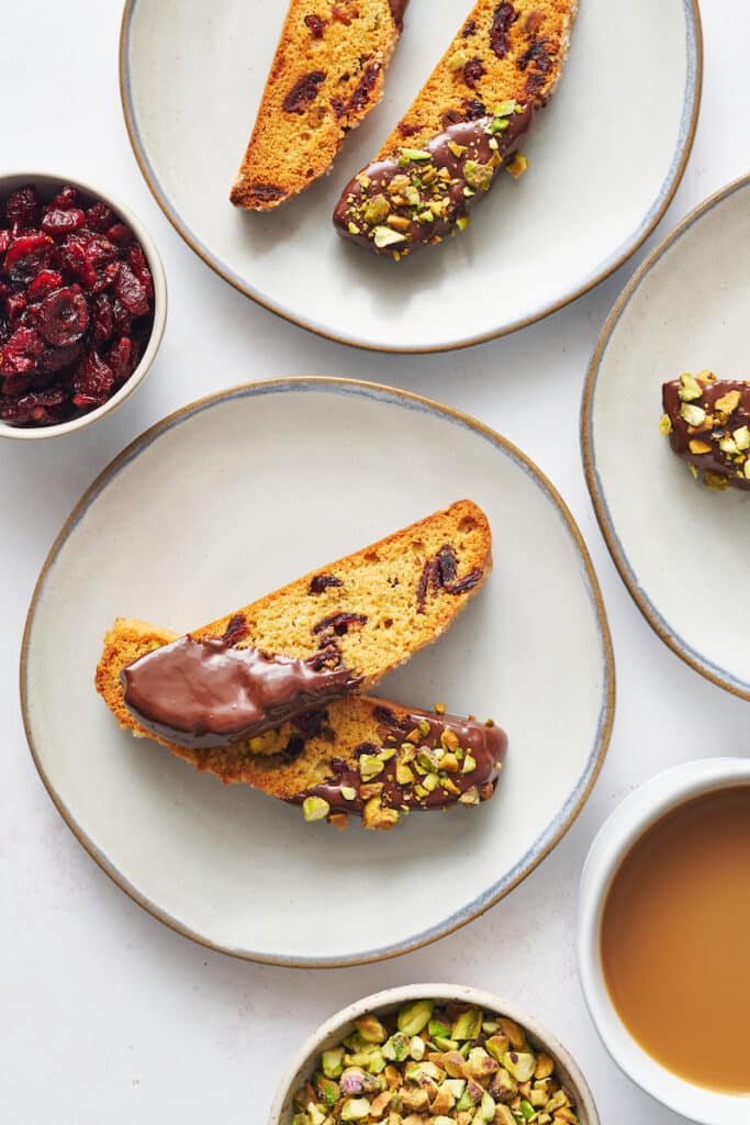 Cranberry pistachio biscotti on a dessert plate with a cup of coffee on the side.