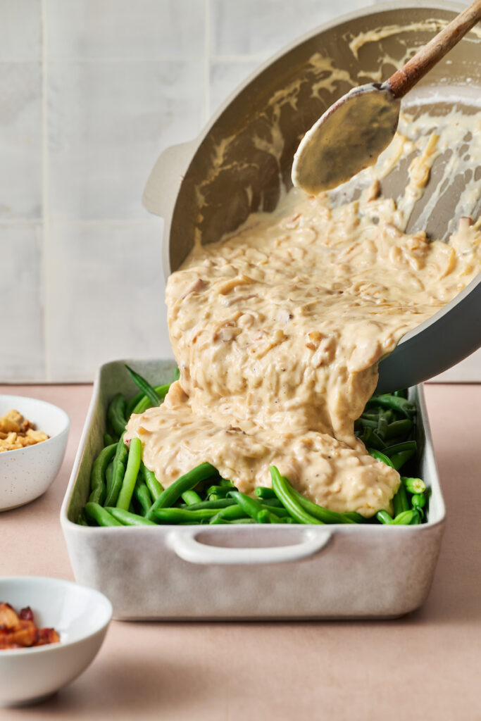 Cheese sauce being poured on top of blanched fresh green beans.