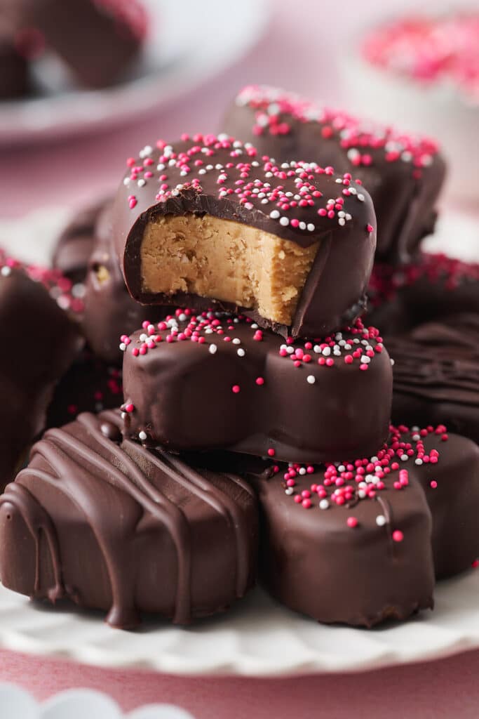 Peanut butter hearts stacked on a plate with a bite taken out of one. 