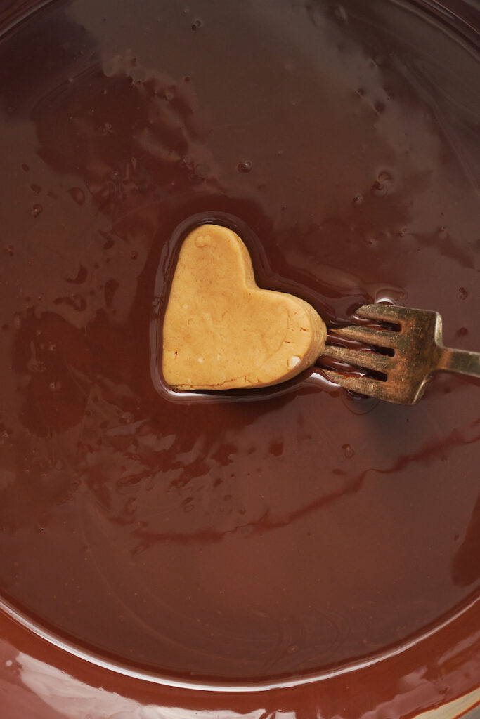 Dipping peanut butter hearts into melted chocolate.