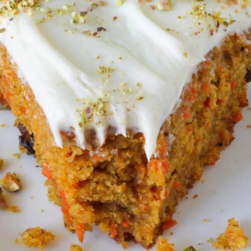 A slice of pumpkin carrot cake with a bite taken out of it. Cream cheese frosting on top with pistachios.