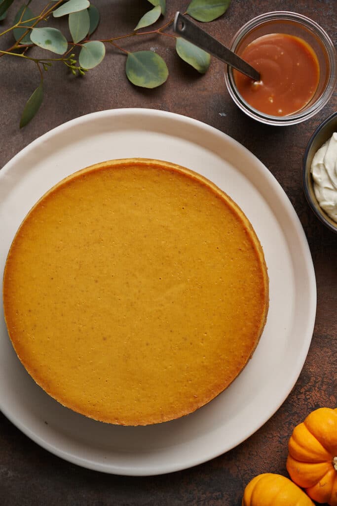 Pumpkin cheesecake on a large plate with whipped cream and caramel sauce on the side.