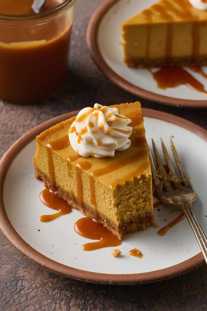 Slice of pumpkin cheesecake on a plate with a bite taken out of it.