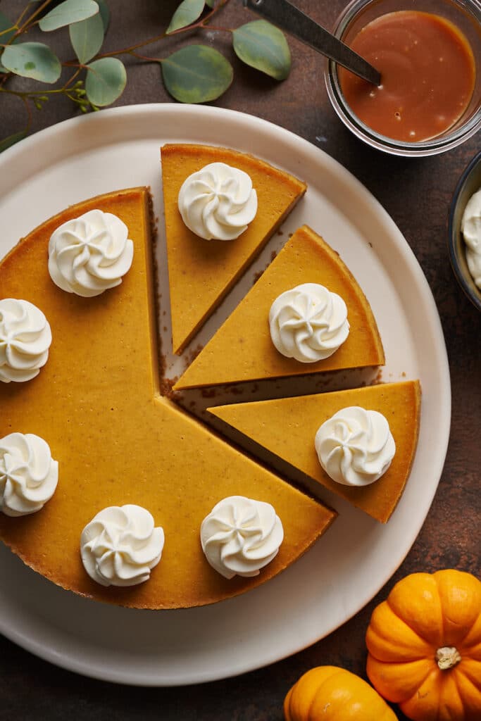 Pumpkin cheesecake on a plate topped with whipped cream and caramel sauce on the side.