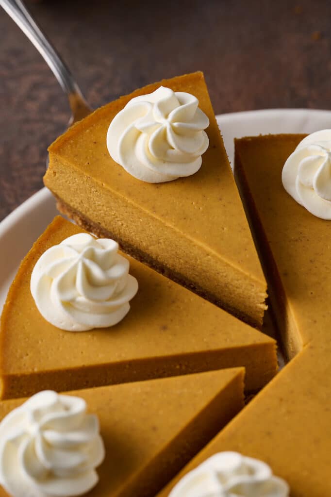 Slice of pumpkin cheesecake being lifted from the tray with a cake server.