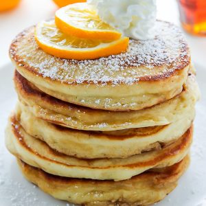 A stack of lemon ricotta pancakes with whipped cream on top.