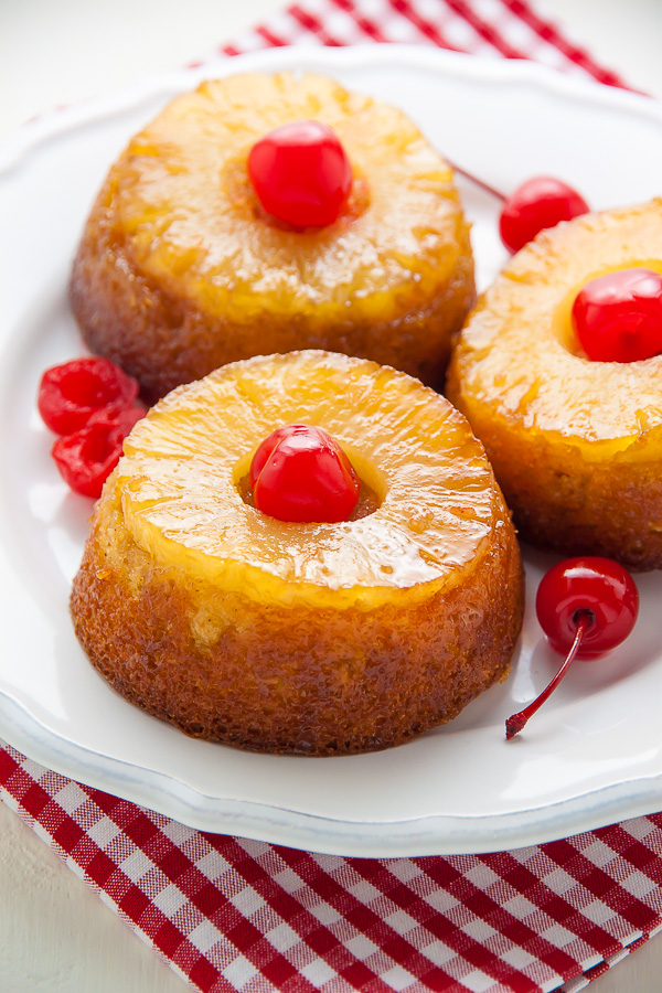 Individual pineapple upside-down cakes on white plate with checkered napkin. 