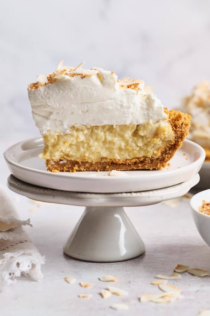 Coconut cream pie on a dessert plate with whipped cream on top.