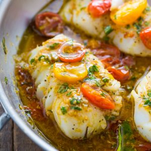 Cod fish in a skillet covered with tomato basil sauce.