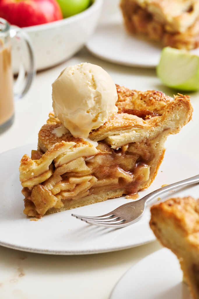 Slice of apple pie on a plate with ice cream on top.