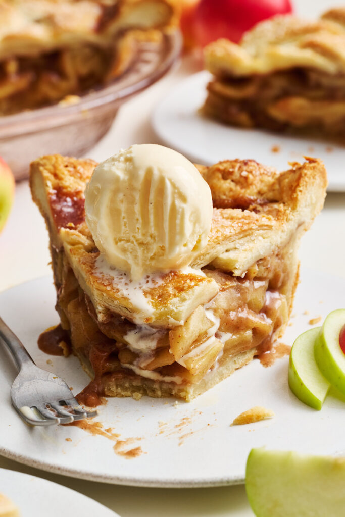 Slice of apple pie on a dessert plate. With a bite taken out and ice cream on top.