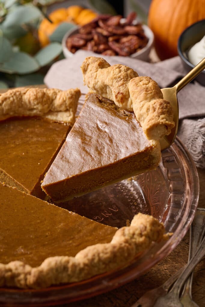 Pumpkin pie being removed from the pie plate with a server.