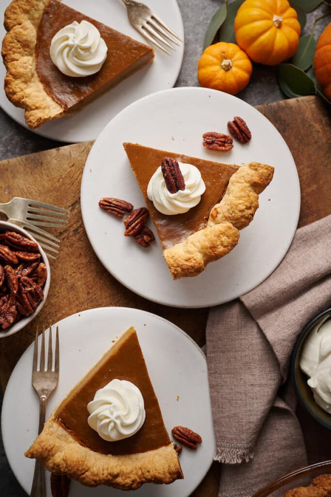 Slices of pumpkin pie with whipped cream and candied pecans on top.