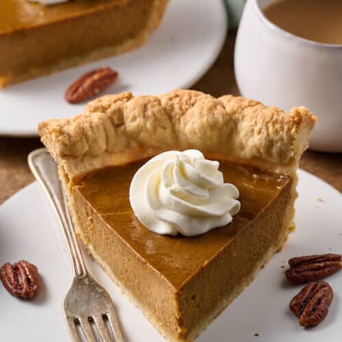 Slice of pumpkin pie on a plate with whipped cream on top.