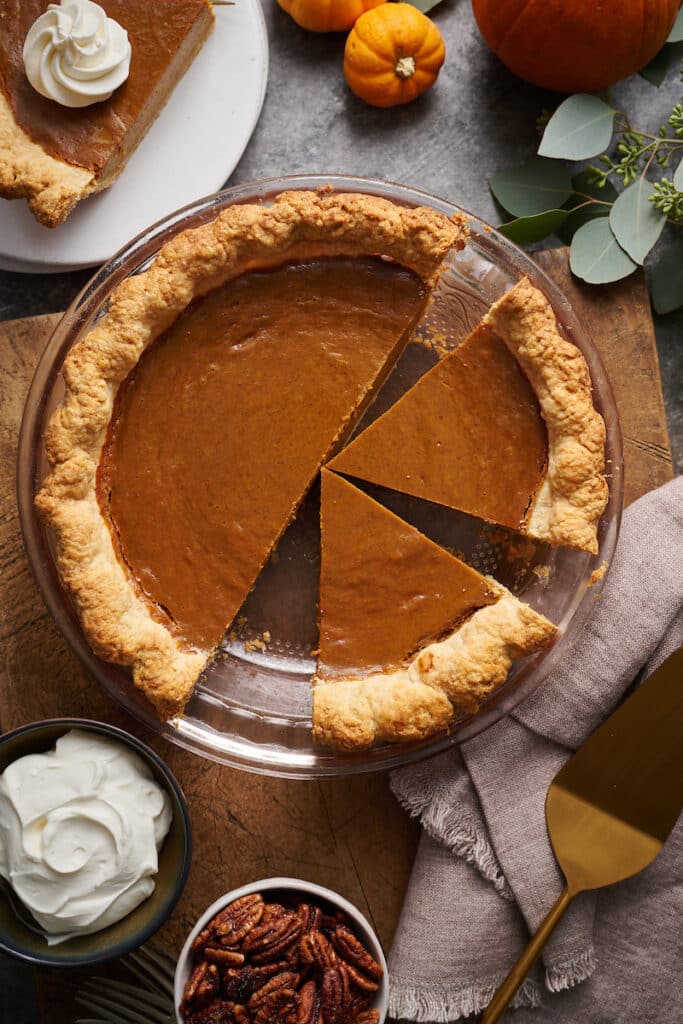 Pumpkin pie in a pie plate with whipped cream and candied pecans on the side.