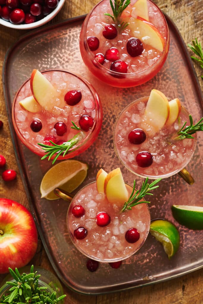 a tray with cranberry Moscow mules garnished with fresh cranberries a sprig of rosemary.