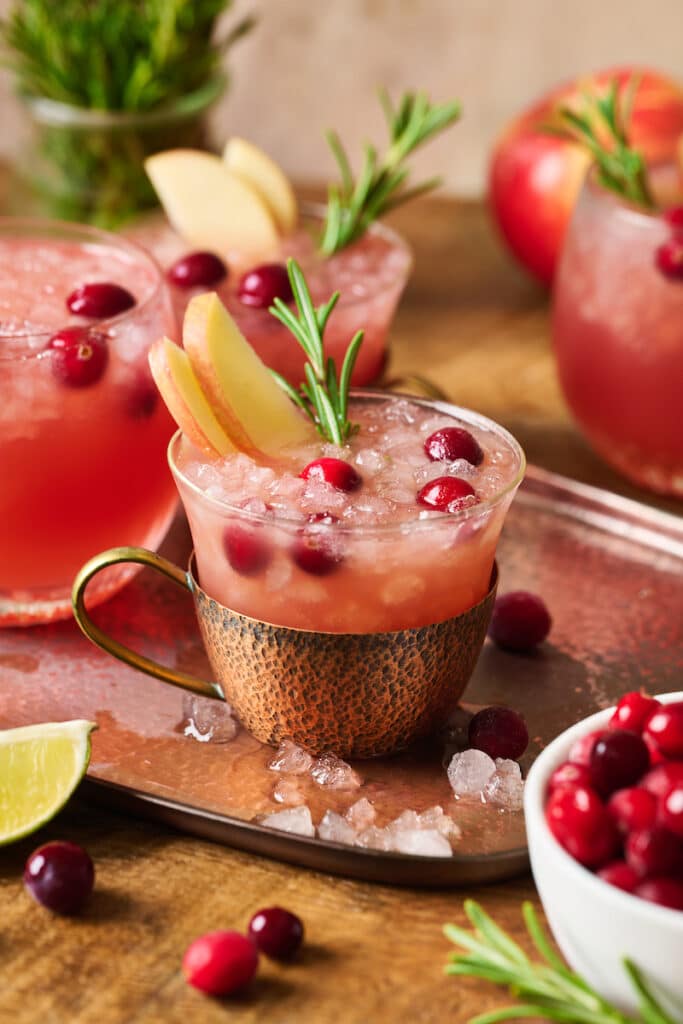 Tray with cranberry Moscow Mule garnished with a sprig of rosemary and fresh cranberries.