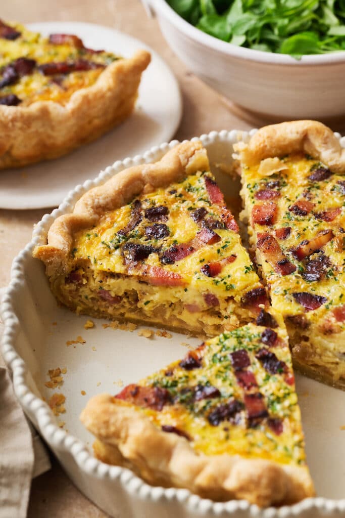 Quiche Lorraine in a pie plate sliced up with bacon on top.