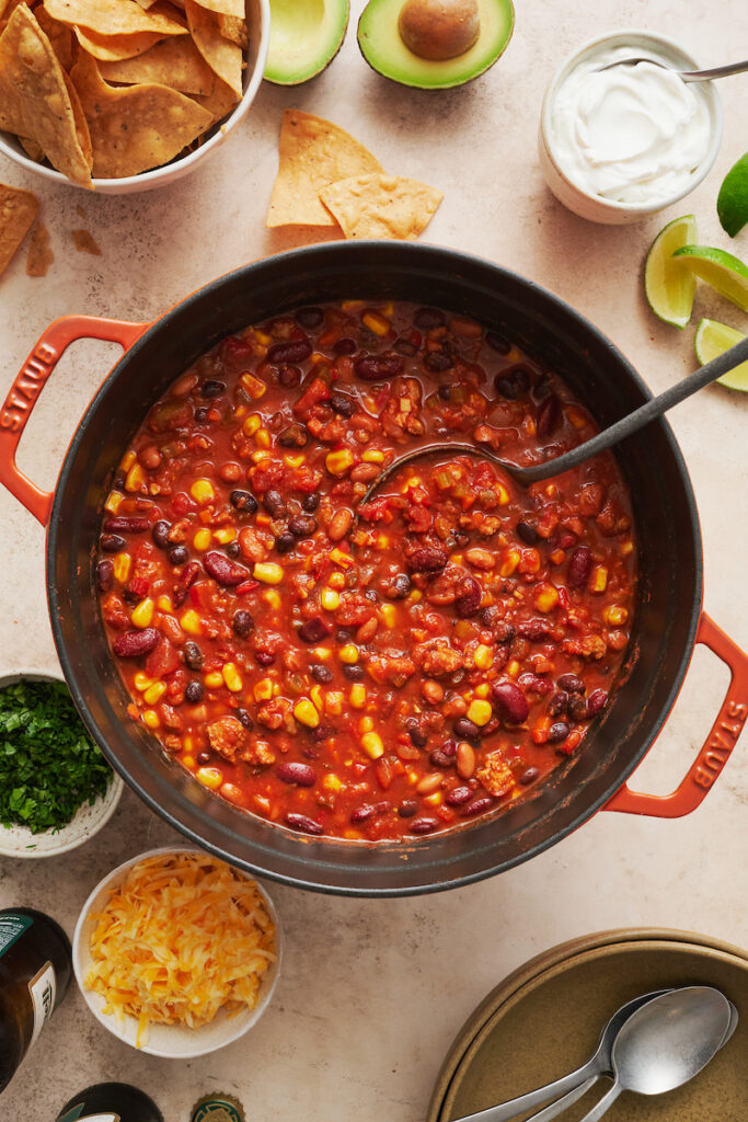 Pot of turkey chili with ladle in the pot and garnishes on the side.