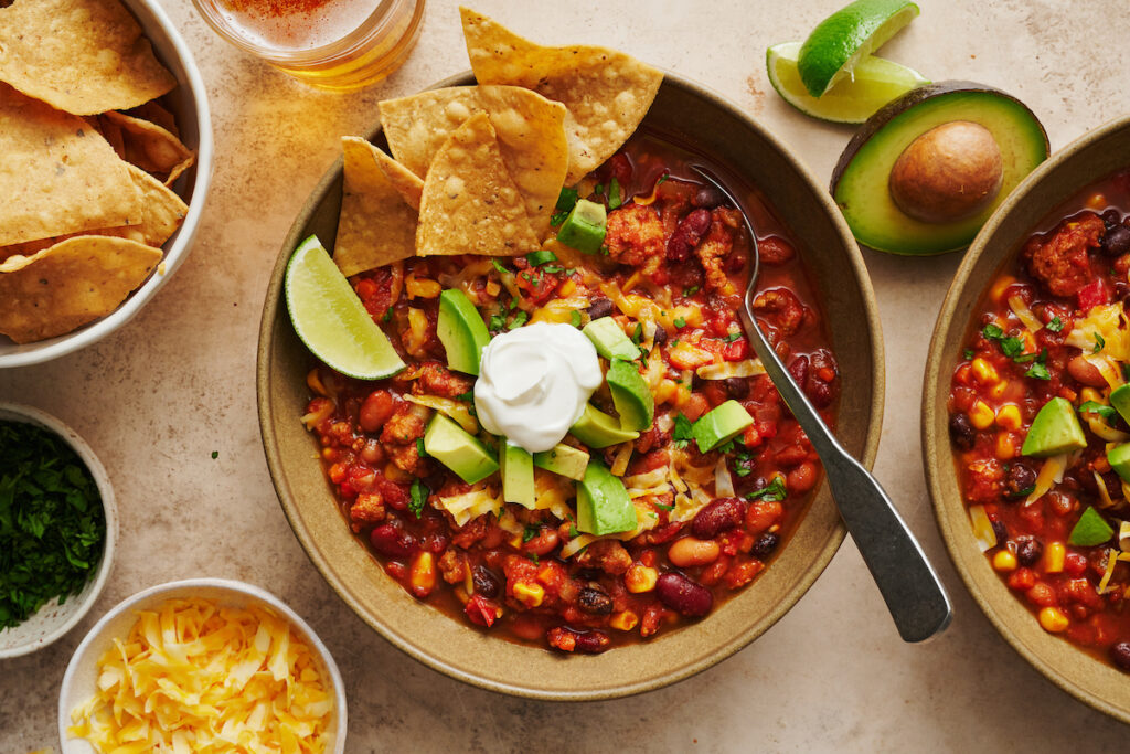 Bowl of turkey chili with tortilla chips and lime wedges.