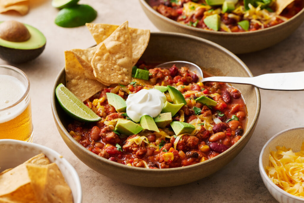 Turkey chili in bowls with tortilla chips, avocado, and sour cream.