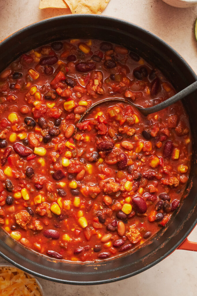 A big pot of turkey chili in a dutch oven with a ladle. 