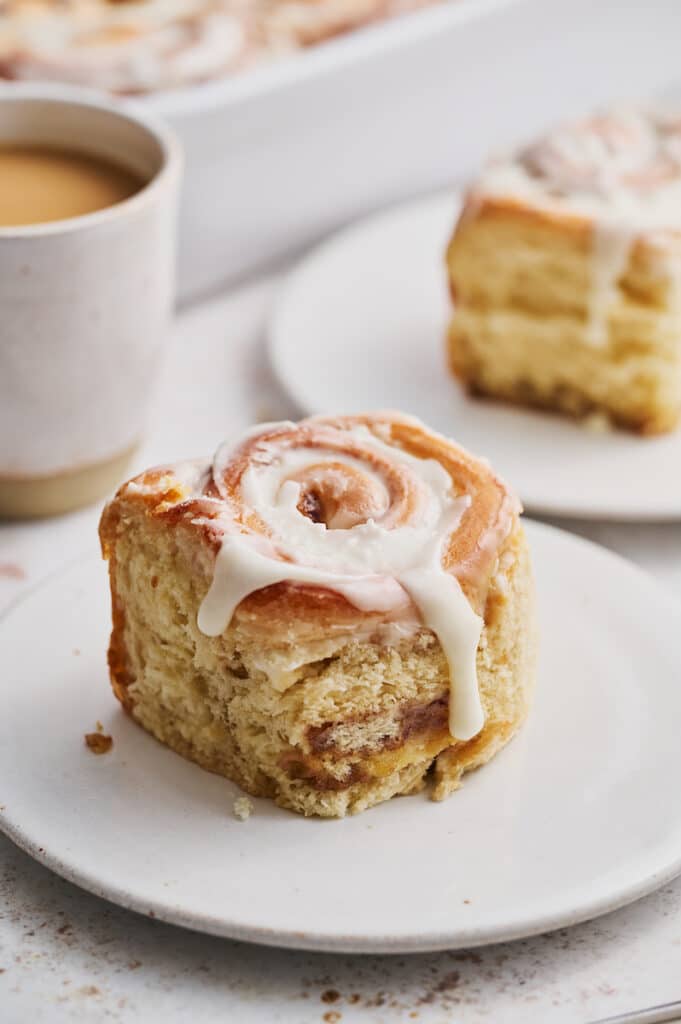 Cinnamon roll on dessert plate with a cup of coffee on the side.