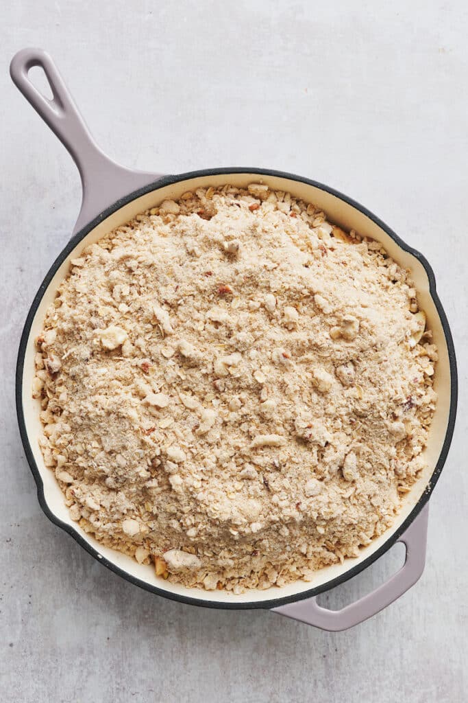 A skillet of apple filling topped with crumbly topping for apple crisp recipe.