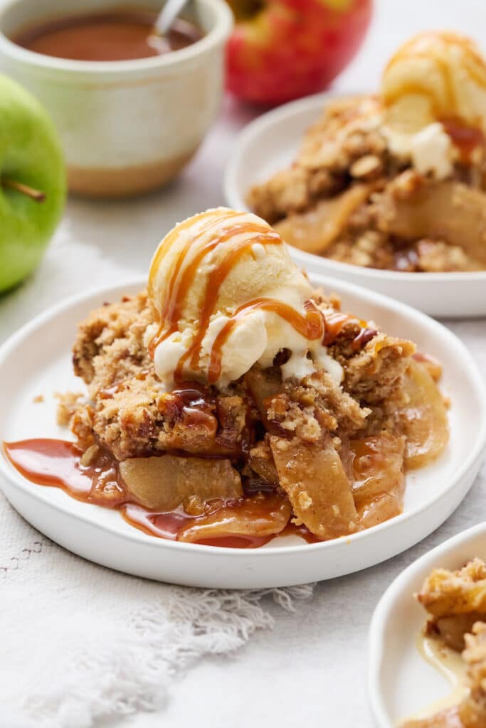 Apple crisp topped with a drizzle of caramel sauce and vanilla ice cream. on a plate.