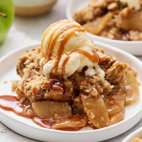 Apple crisp topped with a drizzle of caramel sauce and vanilla ice cream. on a plate.