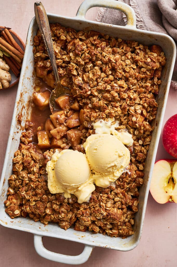 Rectangle pan wit apple crisp inside and scoops of vanilla ice cream on top.