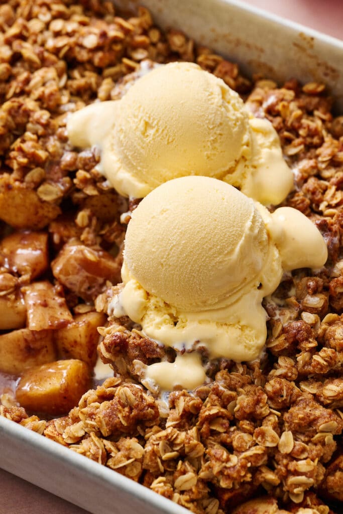 Baking dish with apple crisp inside and scoops of vanilla ice cream on top.