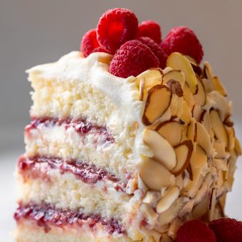 A slice of white chocolate raspberry cake with fresh berries on top.