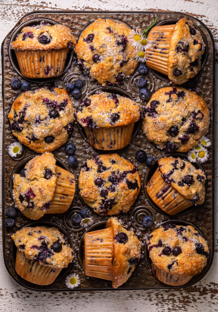 Muffin tin with banana blueberry muffins and tiny flowers. 