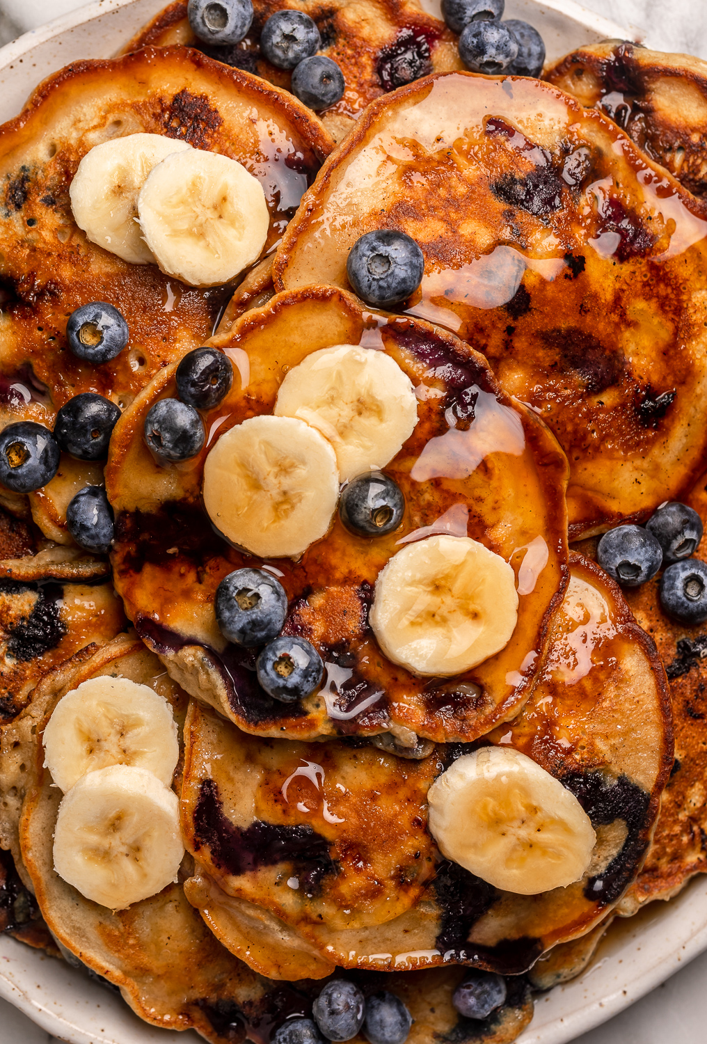Ripe bananas and fresh blueberries make these Banana Blueberry Pancakes tender, fluffy, and flavorful! The pancake batter comes together in just minutes, and is quickly cooked to golden brown on a hot skillet. Top with maple syrup, extra blueberries, and banana slices for a beautiful breakfast at home!