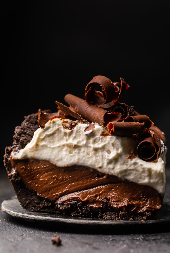 Chocolate pudding pie on a plate with whipped cream and chocolate shavings.