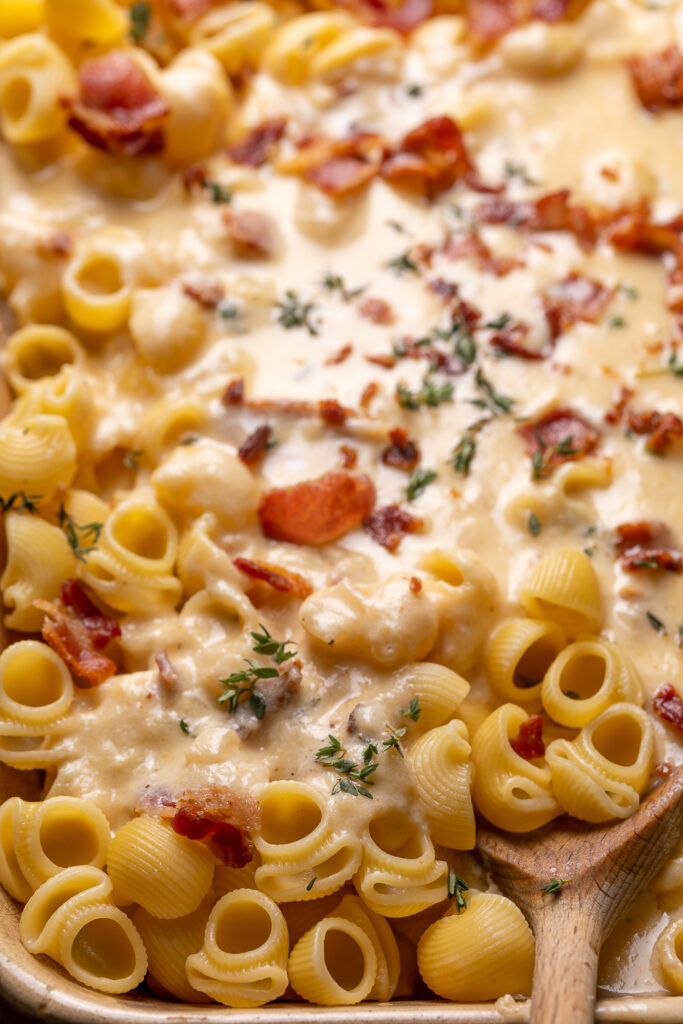 Cooked pasta being mixed with creamy cheese sauce for baked macaroni and cheese recipe.