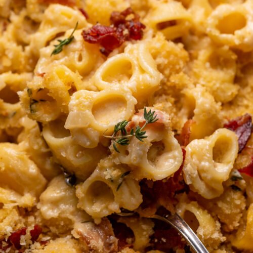 Baking dish with macaroni and cheese topped with bacon and thyme.