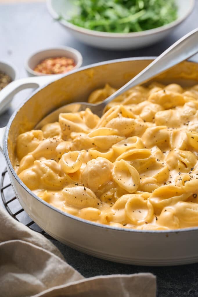 Homemade Mac and cheese in a skillet with a spoon and salad on the side.