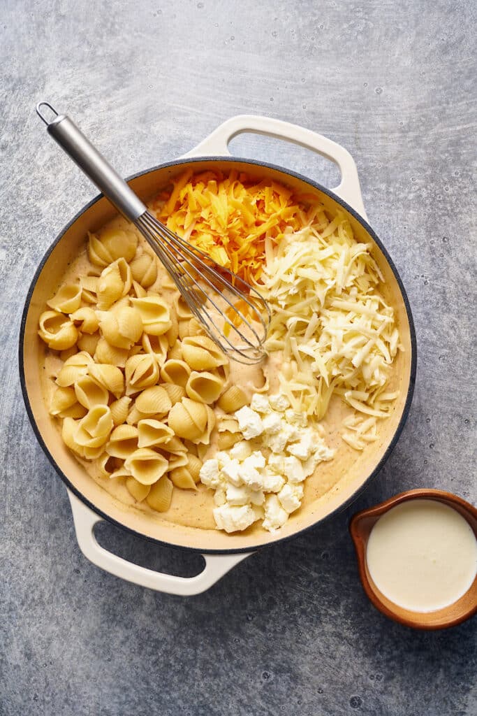 Ingredients for homemade macaroni and cheese including shredded cheddar cheese and cream cheese in a skillet. 