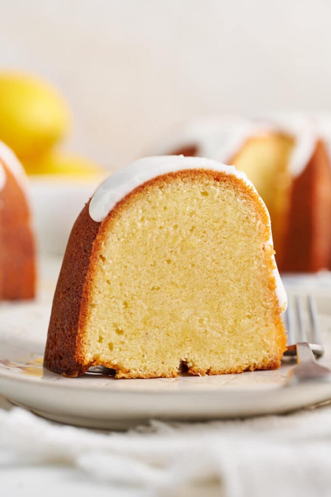 Slice of lemon bundt cake on white plate a bite taken out of the cake.