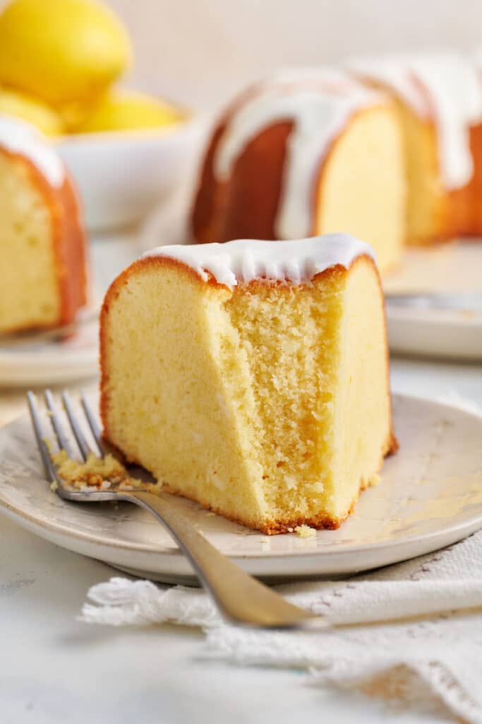 Slice of lemon bundt cake on white plate a bite taken out of the cake. 