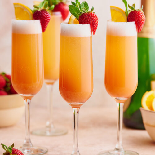 Todo mundo sabe fazer uma mimosa clássica, então hoje estou ensinando como fazer minha receita especial de mimosa de morango ao nascer do sol!  Feitos com purê de morango, champanhe e suco de laranja espremido na hora, são perfeitos para o brunch!  Enfeite com raminhos de hortelã, morangos e rodelas de laranja para uma apresentação ainda mais bonita!