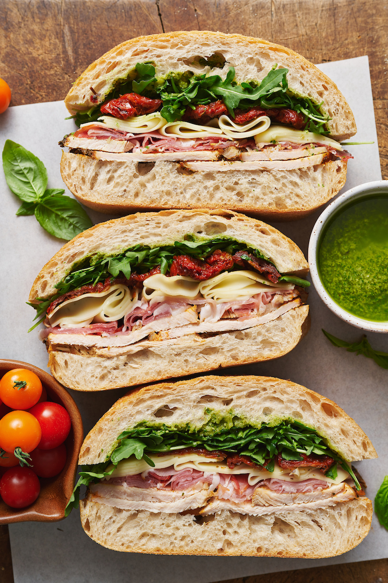This crowd-pleasing Italian Turkey Club Sandwich is perfect for picnics, parties, or those nights it's just too hot to cook! Loaded with sliced turkey, prosciutto, arugula, sun-dried tomatoes, and a homemade Italian dressing, this recipe is so flavorful and fresh. So without further ado, let's make sandwiches!