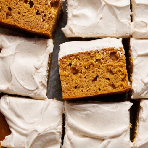 Pumpkin cake topped with cream cheese frosting sliced into squares.