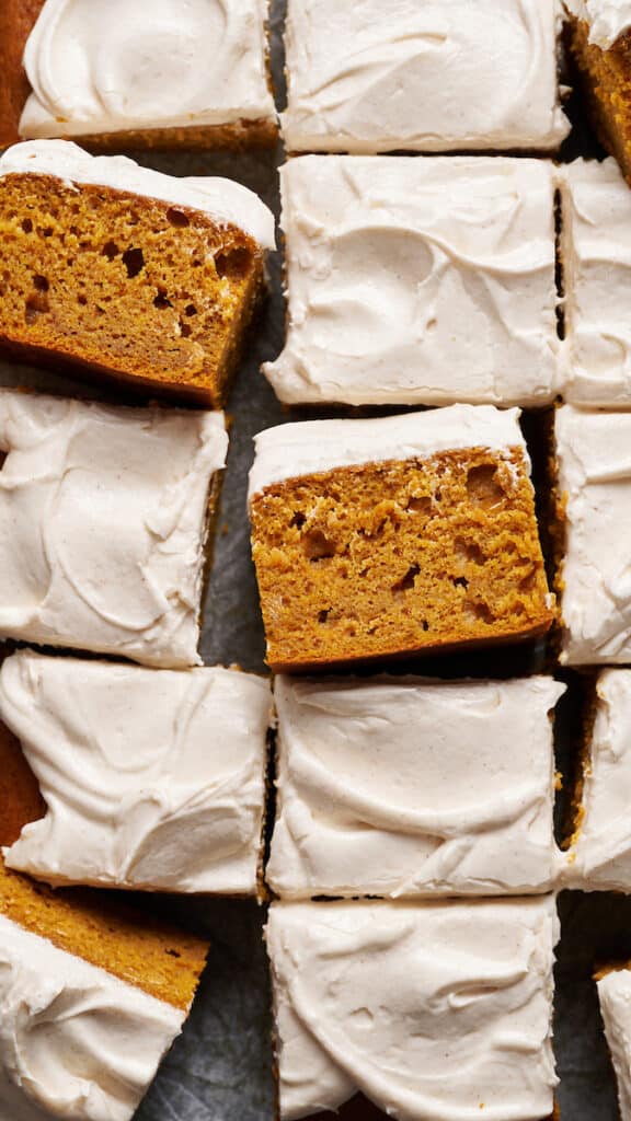 Pumpkin cake topped with cream cheese frosting sliced into squares. 